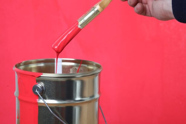 A person pouring bright red paint from a glass tube into a metal can against a red background.