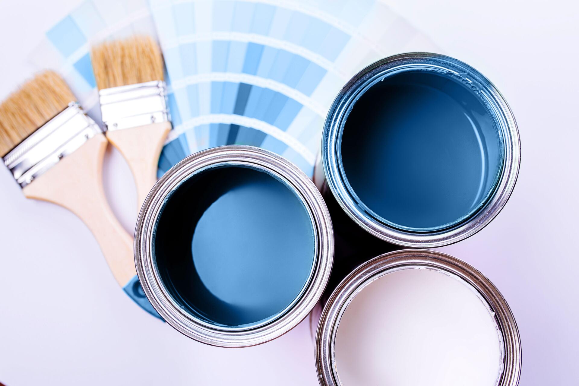 Top view of three open paint cans in shades of blue and white, with paintbrushes and a color swatch guide on a white background.