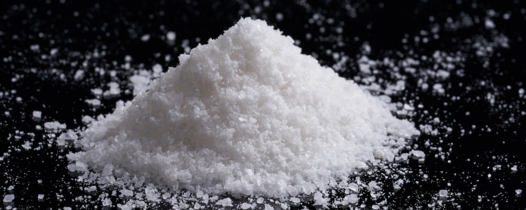 An image of about 200 grams of caustic soda or sodium hydroxide powder, which is white on a black background