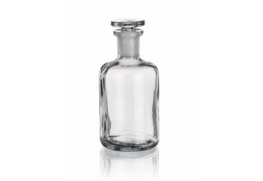 A clear, empty glass bottle with a round body, straight sides, and a wide mouth, topped with a matching glass stopper. The bottle is sitting upright against a plain white background.