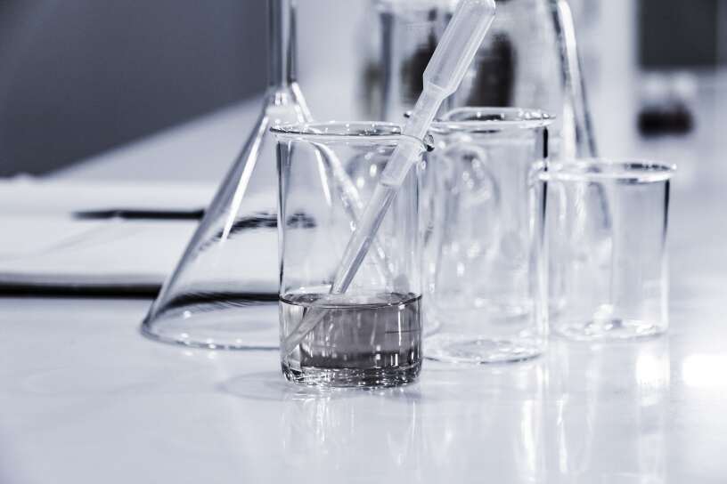 Various glass beakers and a pipette with liquid on a laboratory table, highlighting a scientific experiment setup. the focus is on a beaker being filled.