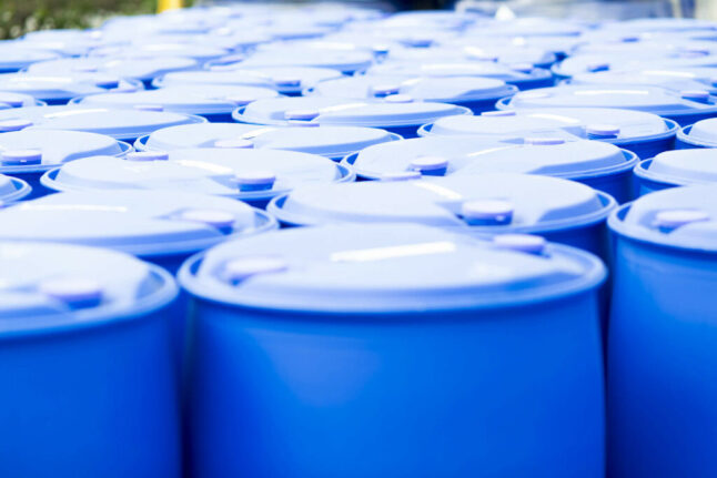 An image of a large number of standard chemical barrels with their lids sealed, each containing industrial grade chemicals in powder or liquid form.