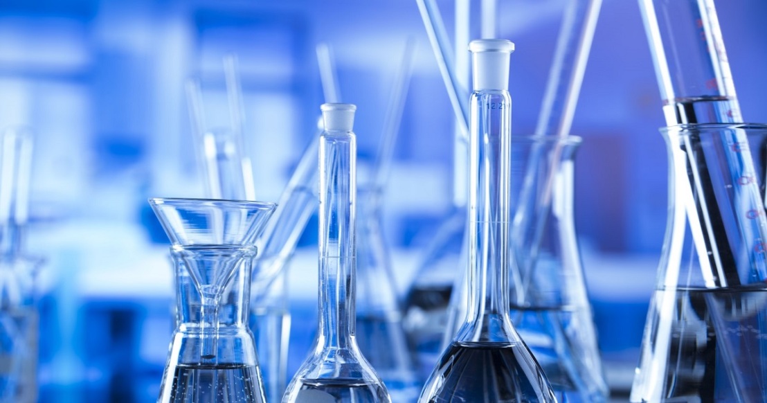 Various glass laboratory equipment, including beakers, flasks, and test tubes, filled with liquids, on a table with a blue-toned background.