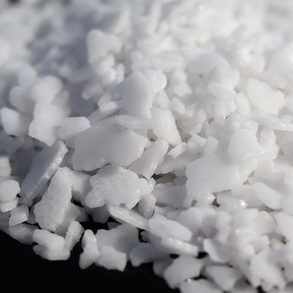 Close-up image of coarse white sea salt crystals against a dark background, showing their irregular shapes and rough texture.