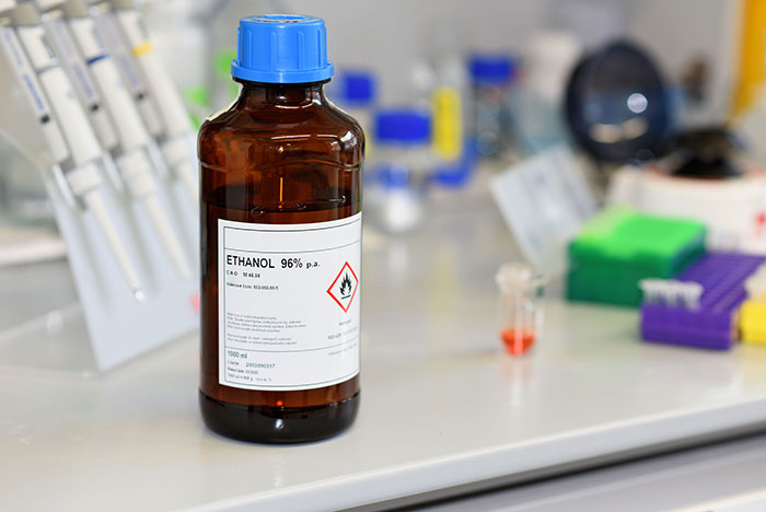 A brown laboratory bottle with a blue lid on the laboratory table with a label of 96% ethanol