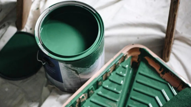 Open can of green paint with a paint roller and tray on a tarp, indicating preparation for a painting project.