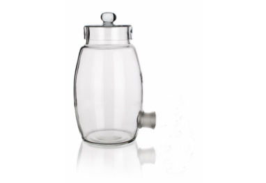 A clear, empty glass jar with a knobbed lid and a spout near the base. The jar is cylindrical with a slight taper towards the top, standing on a reflective white surface.